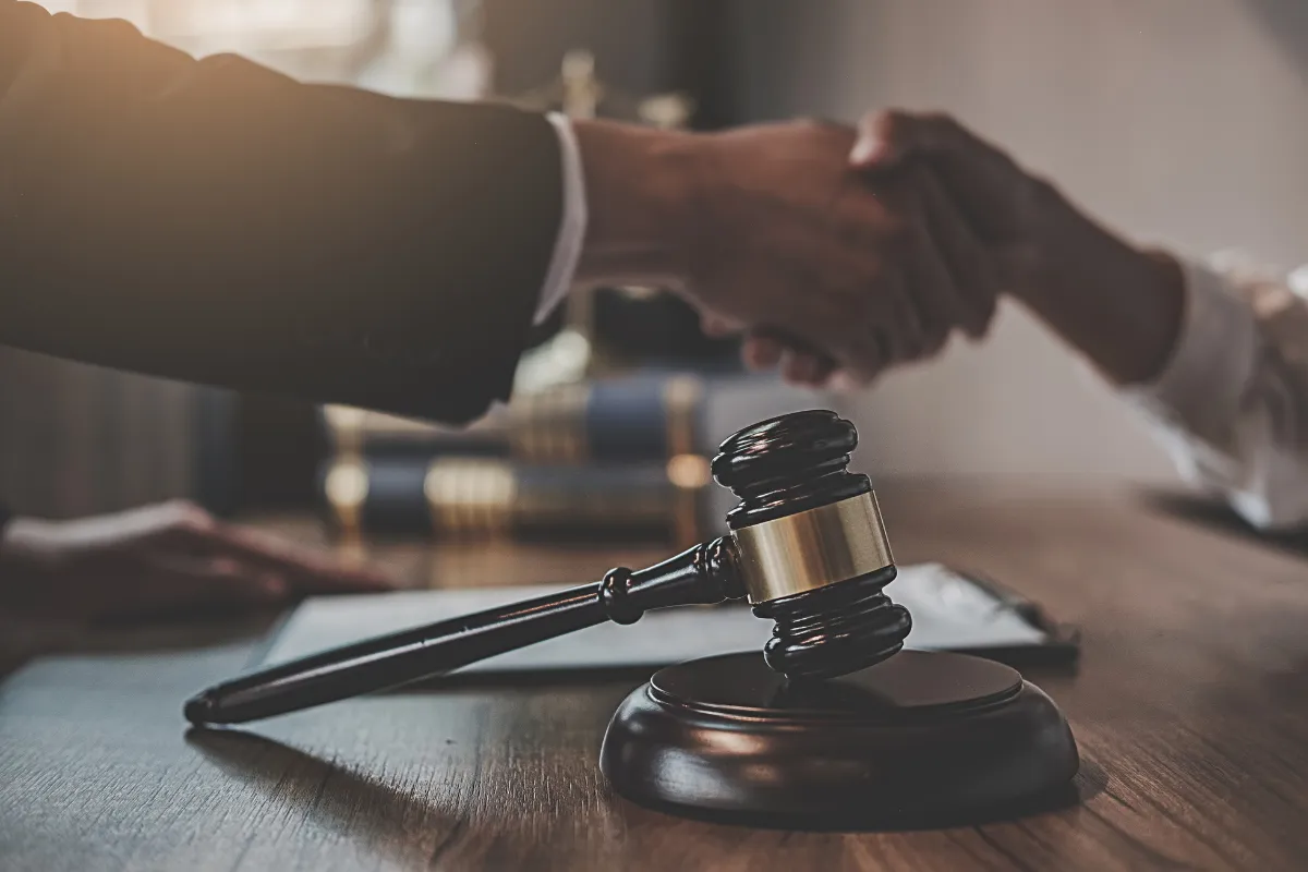 Image showing two hands shaking over a judge's gravel on a table with papers.